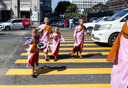 In Myanmar the Buddhist nuns wear pink robes, to distinguish themselves from the monks. Here they cross the road on a street in Yangon.The nuns have been collecting alms. Myanmar, Asia, street, nuns, culture, buddhism, Simon Bond.