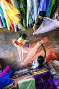 Fabric vendors roll up some material at a market in the centre of Yangon in Myanmar. This is at the Bogyoke Aung San Market. Myanmar, street, photography, colourful, market, asia, travel, photography, Simon Bond.