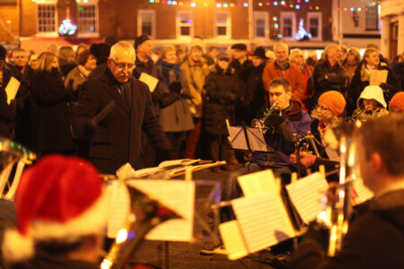 An outdoor carol singing service held in Romsey in the UK before Christmas. A brass band is there for the festive spirits. UK, England, Hampshire, Romset, Carol singing, outdoors, Christmas, culture, tradition, street photography, Simon Bond.